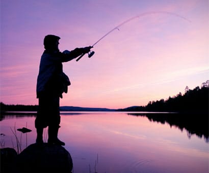 Fisherman casting into water over sunset
